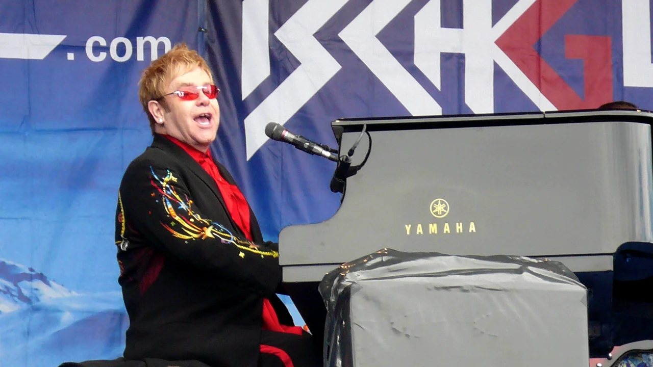 Elton John saluda a los hinchas de Watford en el estadio Vicarage Road, con una bufanda del club en la mano.