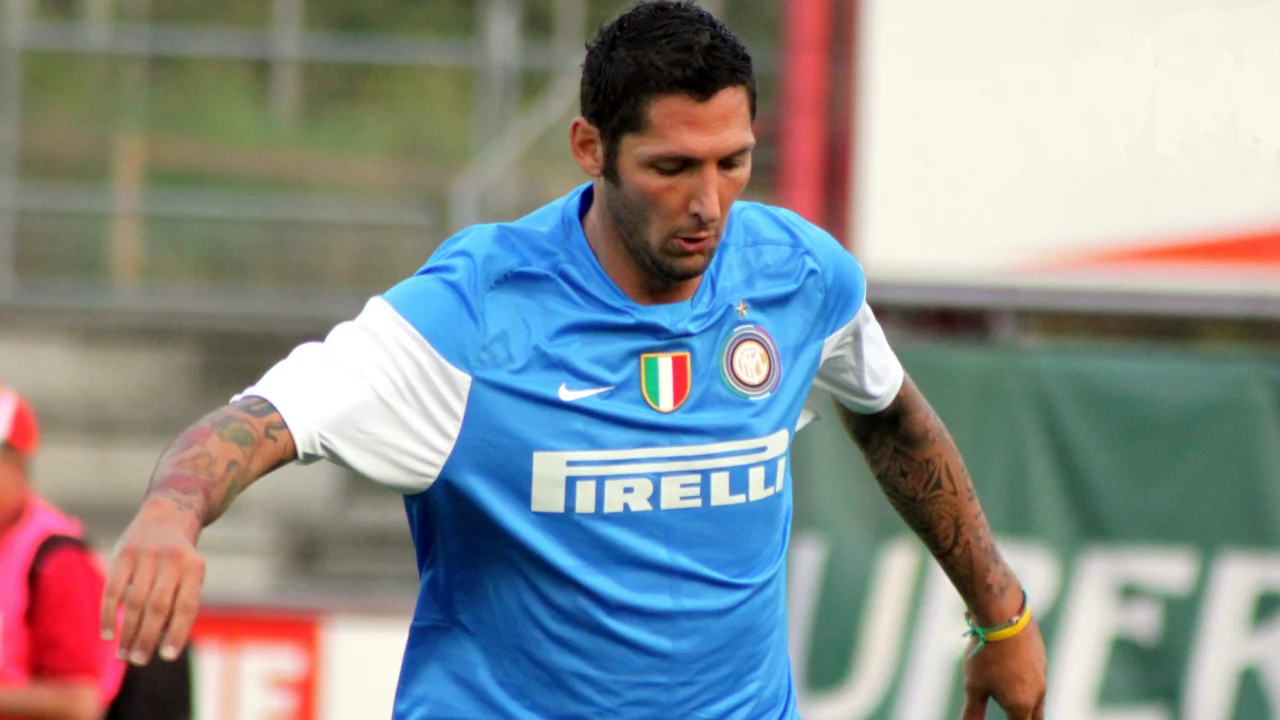 Marco Materazzi apoya su codo sobre el hombro de Rui Costa en el césped de San Siro, con humo de bengalas de fondo.