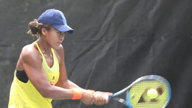 Naomi Osaka durante un partido de tenis, con la raqueta en mano y gesto de concentración.